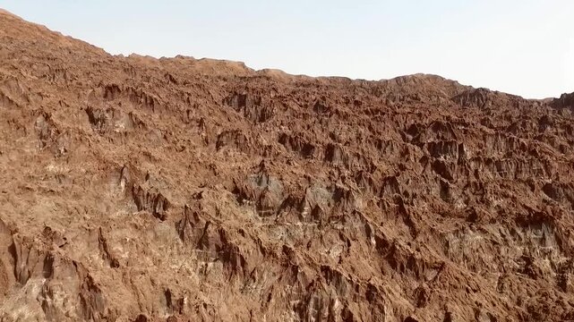 Fascinating macro aerial view tracking along the sharp jagged cliffs and craggy rock faces of a massive salt dome structure, highlighting rich geographical textures and earthly soil erosion.