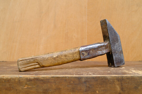 Old rusty hammer lying on vintage wood workbench background