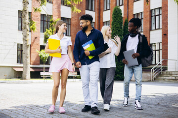 Fototapeta premium University students of different ethnicities walking together on college campus, talking and learning, holding books and laptops