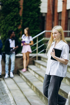 Student holding a notebook, walking down school stairs with other students in the background, representing education and college life