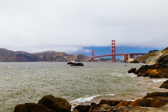 Iconic Golden Gate Bridge Over Water Landscape With Coastal Rocks on Cloudy Day