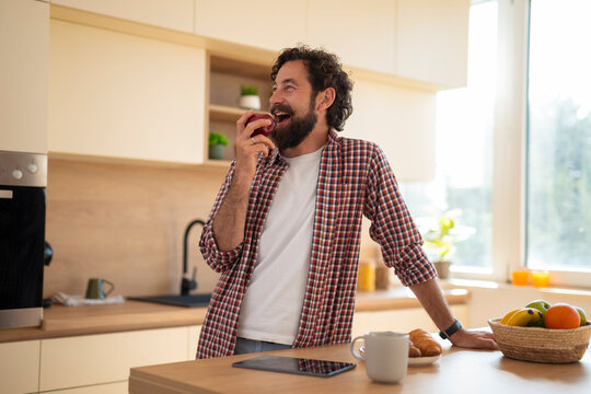Happy man eating apple for healthy breakfast in kitchen