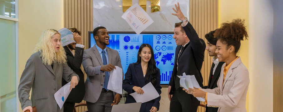 ​A multi-ethnic professional team celebrating a project completion by tossing papers in the air at a modern boardroom, expressing joy, teamwork, and corporate achievement.