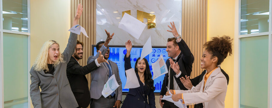 ​A multi-ethnic professional team celebrating a project completion by tossing papers in the air at a modern boardroom, expressing joy, teamwork, and corporate achievement.