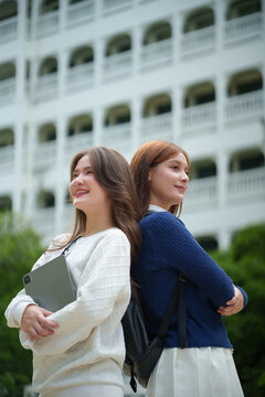 Two confident university students standing back to back on campus with a digital tablet, representing friendship, academic success, collaboration, and modern student life.
