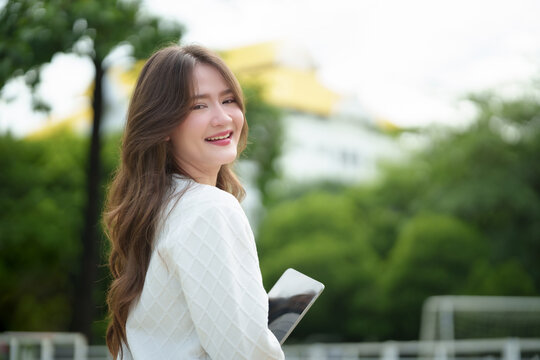 Smiling university student holding a tablet outdoors on campus, representing higher education, academic success, digital learning, and a confident student lifestyle.
