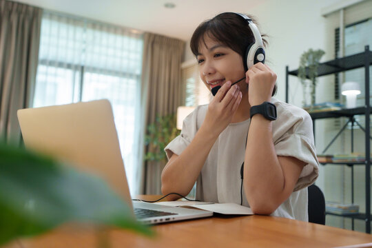 Young woman wearing a headset while studying on a laptop at home, representing online learning, virtual classes, remote communication, and flexible digital education.