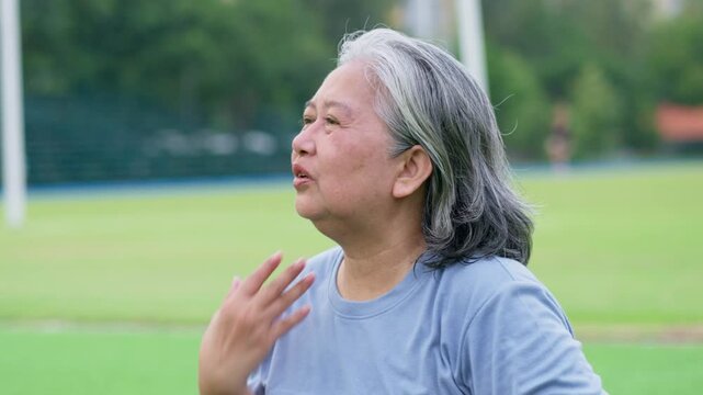 Asian elderly woman outdoors expressing discomfort in hot weather, symbolizing heat wave, El Ni&ntilde;o, climate change, wellness, and lifestyle impact in natural environment with greenery and daylight