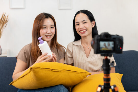 Asian influencer demonstrating skincare cream product during live broadcast, highlighting digital marketing, beauty promotion, and lifestyle branding in cozy home environment with decorative setup