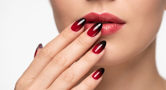 Macro photograph of woman lips and hand with red and black ombre nail extensions