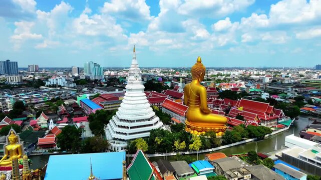 Aerial orbit shot circling around Giant Golden Buddha statue and white pagoda at Wat Paknam, Bangkok, Thailand