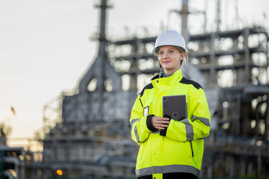 Female industrial engineer holding tablet at oil refinery plant, Refinery technician smiling with device at oil and gas facility, Woman supervisor in safety gear managing operation at industrial plant