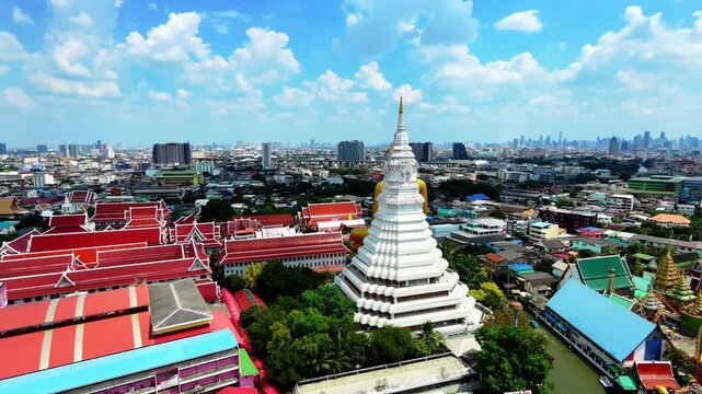 Aerial orbit shot circling around Giant Golden Buddha statue and white pagoda at Wat Paknam, Bangkok, Thailand