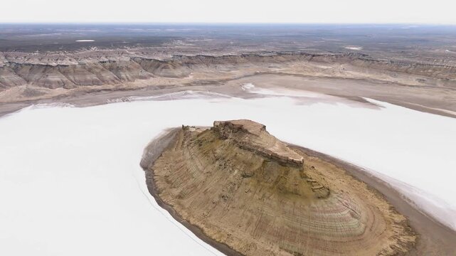 A dramatic close-up drone shot of the iconic Three Brothers rock monoliths standing majestically in the water-covered white salt flat of the Karynzharyk depression in Mangystau, Kazakhstan