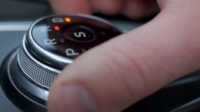 Driver hand turning automatic gear selector in car.