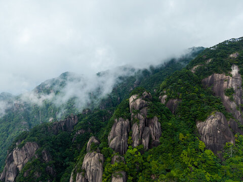 The beautiful granite peaks of Sanqingshan Mountain in Jiangxi China rise above the lush green forest as thick clouds and mist drift slowly across the rocky mountain landscape