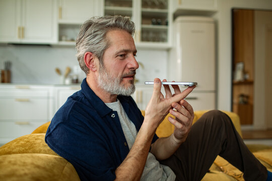 Middle-aged man using smartphone voice assistant at home