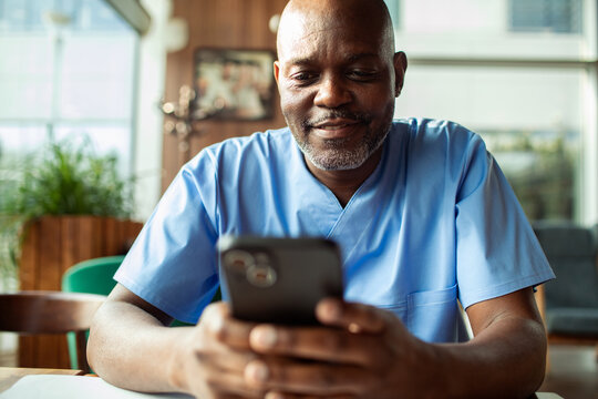 Smiling male healthcare worker using smartphone in hospital breakroom