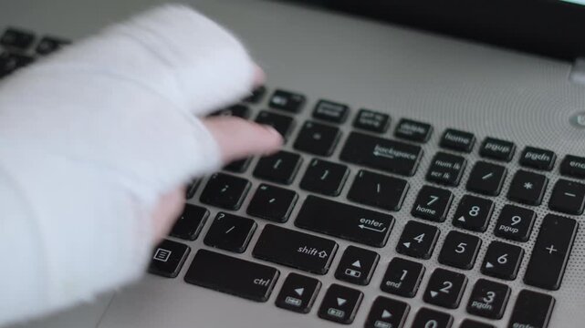 Hand of caucasian child with cast presses Enter key on laptop keyboard. Finger of injured hand of unrecognizable person touches key. Adaptation to circumstances and use of gadgets with limitations.
