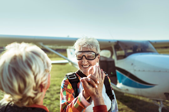 Two senior women high-fiving after skydiving at rural airfield