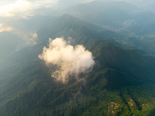 An aerial view captures the green peaks of Sanqingshan Mountain in Jiangxi China as soft white clouds drift over the forest landscape during a bright sunny day © AS_SleepingPanda