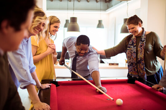 Coworkers playing pool in modern office break room