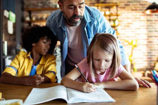 Father helping children with homework at kitchen table