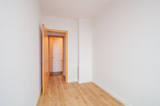 Empty bright room with white walls, light wooden floor and open door leading to adjacent hallway, creating minimalistic interior space for home, apartment or renovation concepts