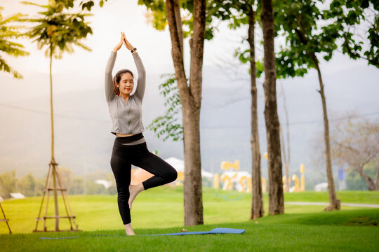 Young Asian woman stretching outdoors during yoga workout in a green park at sunrise