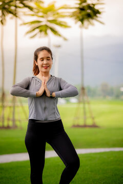Young Asian woman stretching outdoors during yoga workout in a green park at sunrise