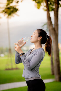 Young Asian woman drinking water after outdoor workout in the park
