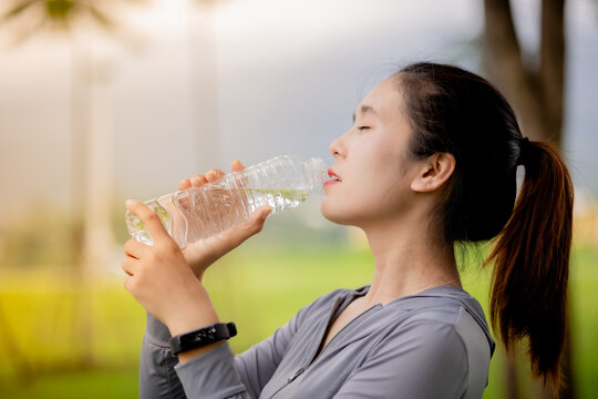 Young Asian woman drinking water after outdoor workout in the park