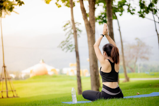 Young Asian woman practicing yoga outdoors in green park at sunrise