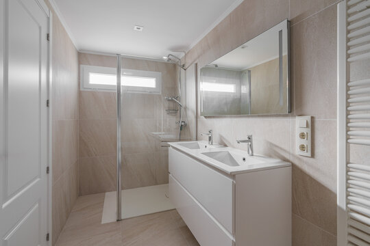 Modern bathroom interior with double vanity, large wall mirror, frameless glass shower, chrome fixtures, beige tile, bright natural light, clean minimalist residential design