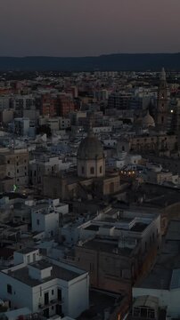 Scenic aerial flight over the ancient city of ostuni in puglia, showing historic architecture, rooftops, and buildings illuminated against the evening sky in italy