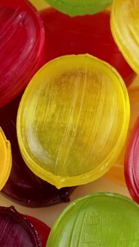 Glossy fruit-flavored hard candies in red, yellow, and green colors circle rotation close up, vertical video
