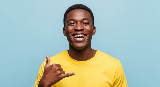 Happy Young African American Man Making Call Me Gesture with Hand, Smiling Broadly on Blue Background