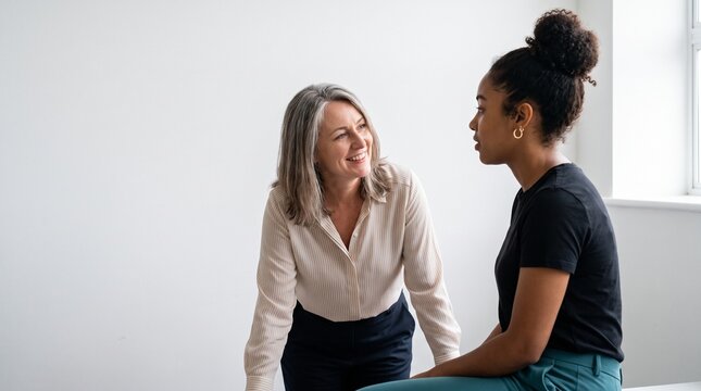 Mature female mentor smiling and talking with a young Black colleague in a modern office setting