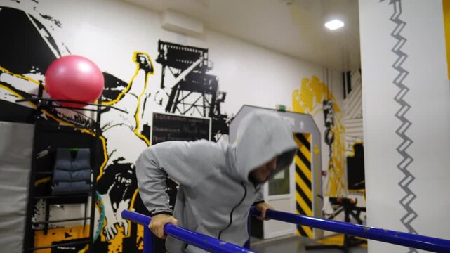 Strong sporty man doing push ups on parallel bars at sport club. Young sportsman exercising at modern gym. Male athlete training hard at fitness centre. Concept of active sportive lifestyle. Close up