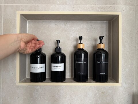 Hand dispensing conditioner from a refillable pump bottle in a built in shower niche with shampoo and body wash containers. Bathroom organization, personal care and sustainable refill concept for home