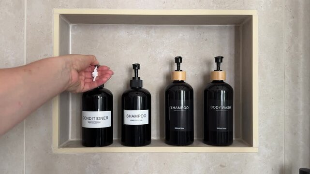 Hand dispensing conditioner from a refillable pump bottle in a built in shower niche with shampoo and body wash containers. Bathroom organization, personal care and sustainable refill concept for home
