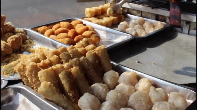 Various Indonesian fried foods, fried tofu, fried tempeh, fried cassava, displayed on street food cart
