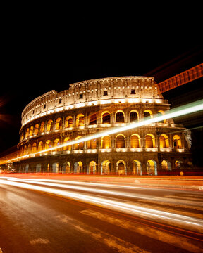 The Colosseum in Rome at night. Illuminated historic Roman amphitheater featuring long exposure traffic light streaks.