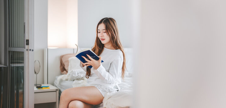 Young adult asian woman reading a book in bedroom home apartment morning routine productivity habit skill leisure
