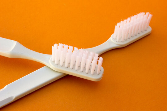 White toothbrushes isolated on orange background. A toothbrush is an oral hygiene instrument used to clean the teeth, gums, and tongue. When paired with toothpaste, it effectively removes plaque, prev
