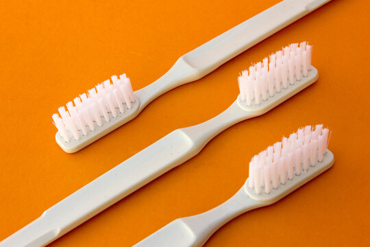 White toothbrushes isolated on orange background. A toothbrush is an oral hygiene instrument used to clean the teeth, gums, and tongue. When paired with toothpaste, it effectively removes plaque, prev