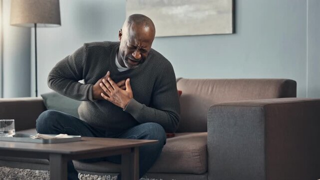 Man experiencing severe chest pain sitting on sofa in modern living room with lamp and artwork