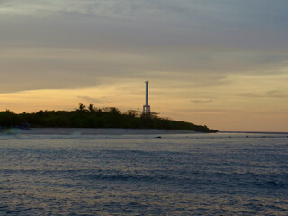 Coastal beacon tower rising above a quiet tropical shoreline at sunset. Soft evening light and calm sea create a peaceful seascape ideal for travel and coastal destination themes. © Houston