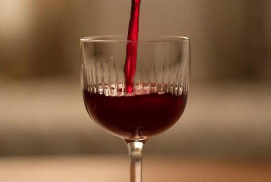 Red Wine Pour: A rich stream of deep red wine cascades into a clear, elegant glass, its ruby hue shimmering in the soft light. A moment of sophisticated indulgence and sensory delight.