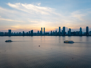 Obraz premium The modern city skyline of Nanchang in Jiangxi China reflects beautifully over the water as boats travel along the river during a peaceful and golden sunset